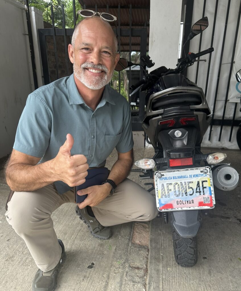 Chris Gibson beside a motorcycle during international travel in Venezuela